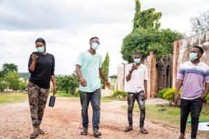 A group of young black friends strolling in the park, wearing face masks, walking apart from each other