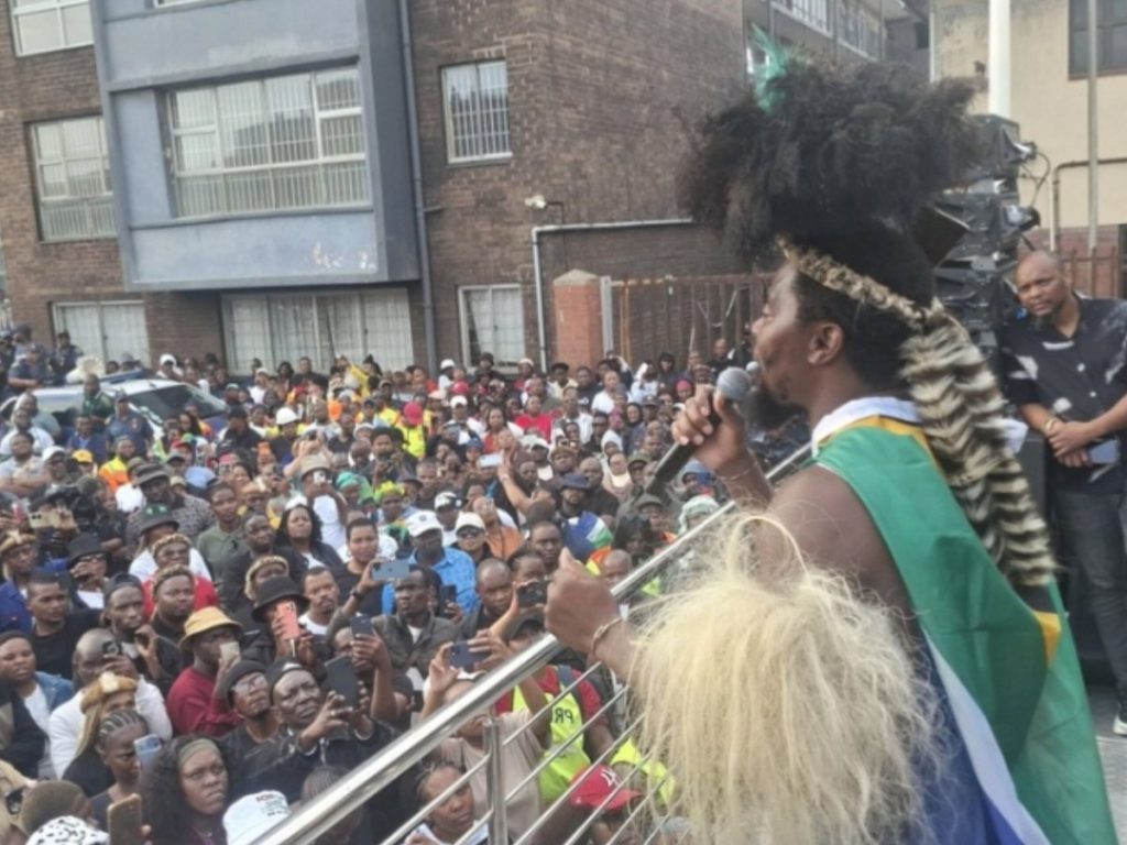 Nkosikhona 'Phakel'umthakathi' Ndabandaba addresses a crowd during the June 30, 2026 Afrophobia marches. Hours earlier, he had met privately with President Cyril Ramaphosa at the Union Buildings, in the absence of Jacinta Ngobese-Zuma, the March and March leader, who said she found out about the meeting on social media. At his press conference the following day, he denied being bribed.