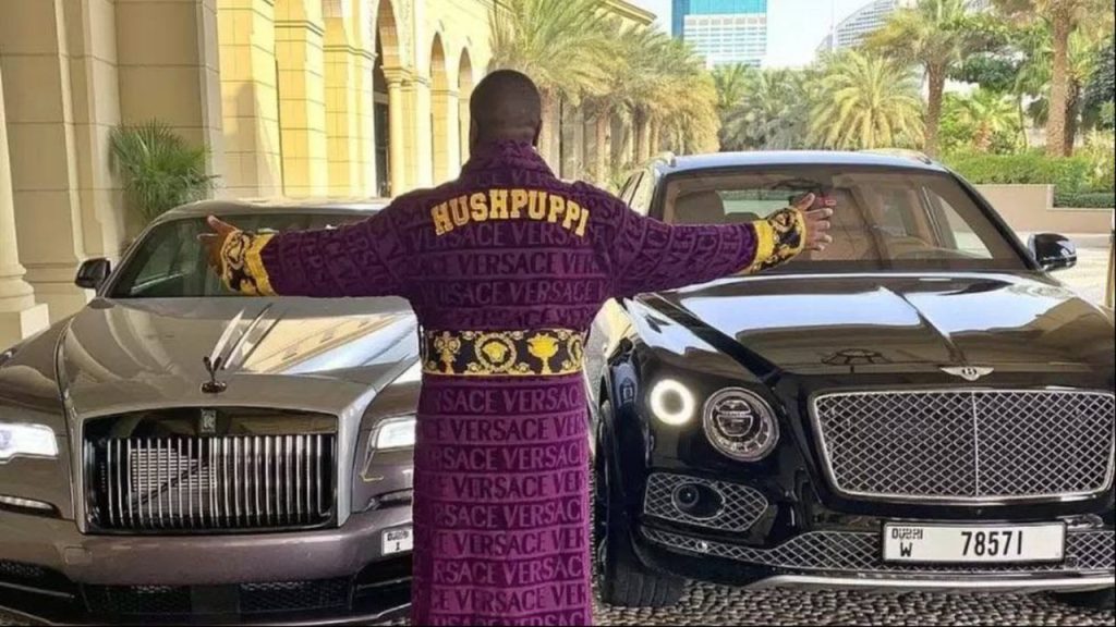 Ramon Abbas, known as Hushpuppi, poses with a Bentley and Rolls-Royce. He was known for living at properties like the Palazzo Versace Dubai, and federal prosecutors later said his lifestyle was funded by over $300 million in laundered money.